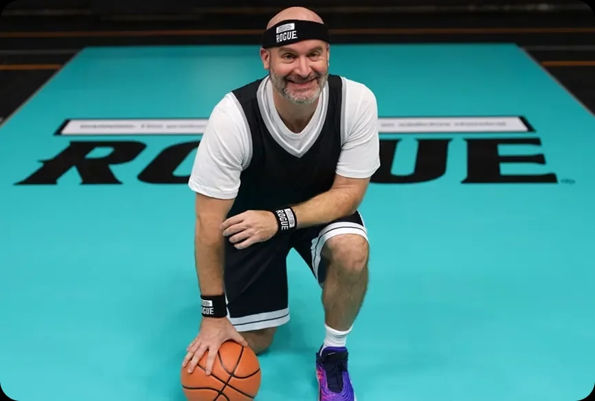 Tom Segura leaning on a basketball with Rogue logo in background